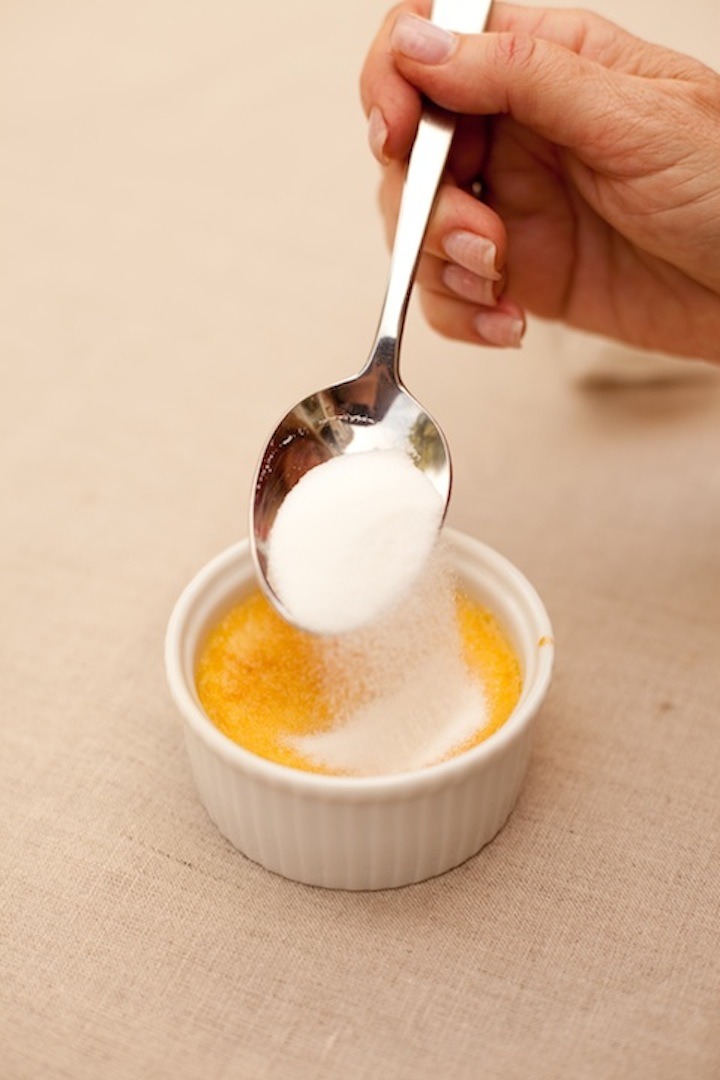 A female's hand holding a spoon and sprinkling sugar on Orange Vanilla Creme Brûlée