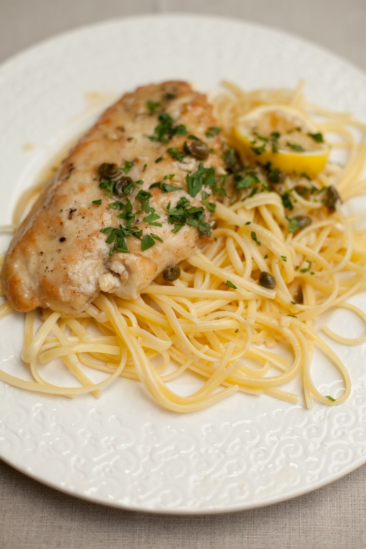 Chicken Piccata on white plate set on a beige table cloth 