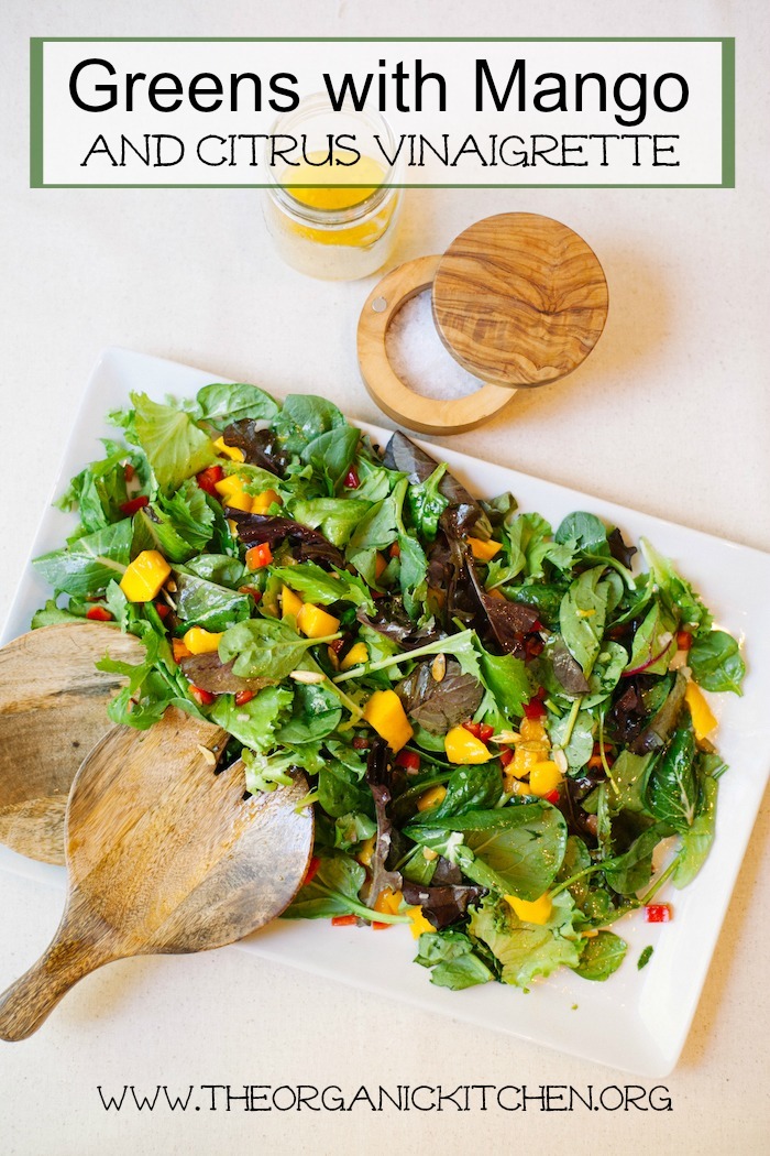 Greens with Mango and Citrus Vinaigrette on a large white platter with a jar of salad dressing and a bowl of sea salt