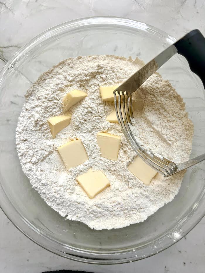 Cubes of butter and flour in a glass bowl with a pasrty cutter