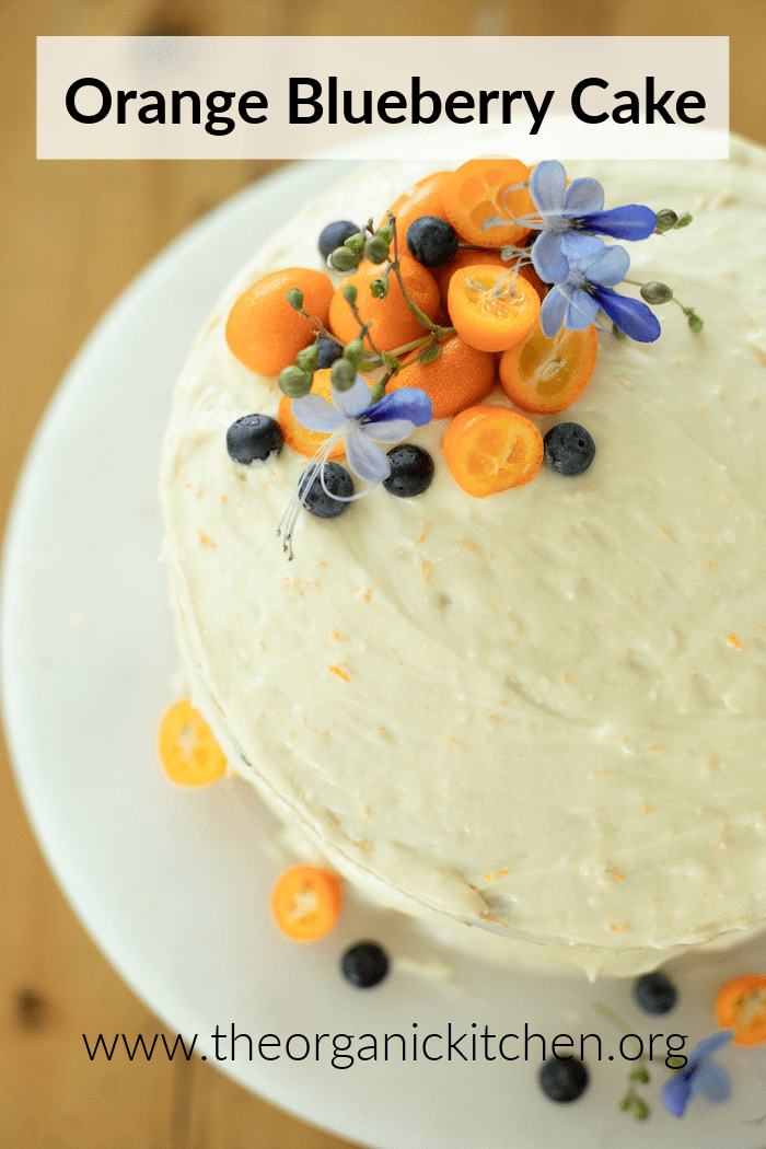 Orange Blueberry Cake with Orange Buttercream Frosting topped with kumquats, blueberries and purple flowers