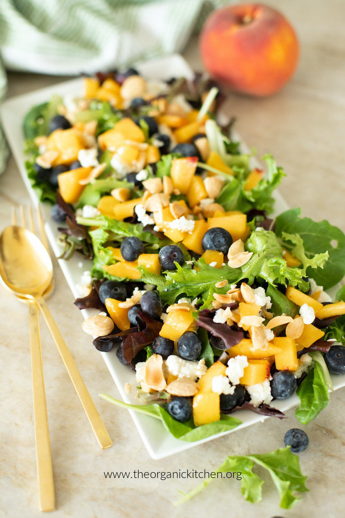 Peach and Blueberry Summer Salad on white plate with green and white dish towel and a peach in background