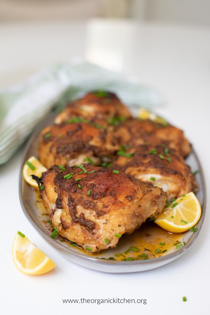 Whole30-Keto Greek Chicken Thighs and lemon wedges on grey plate sitting on a white table