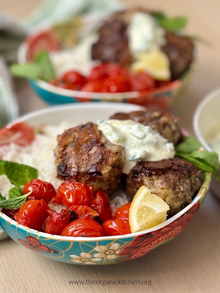 Greek Meatball and Tzatziki Rice Bowls garnished with fresh mint leaves and lemon slices on wooden table