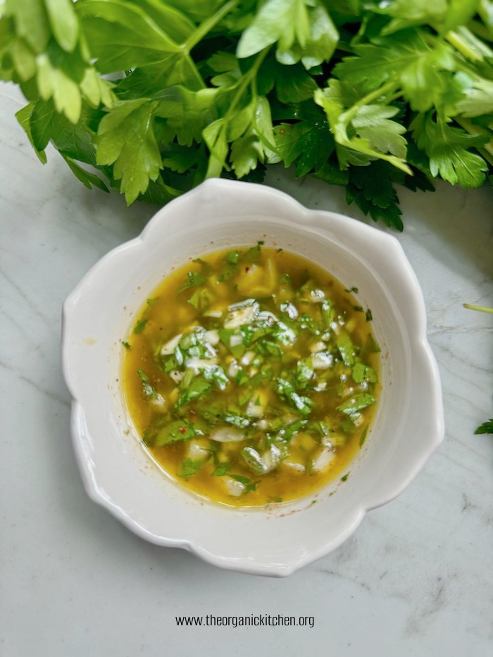 A white bowl of chimichurri sauce on marble table