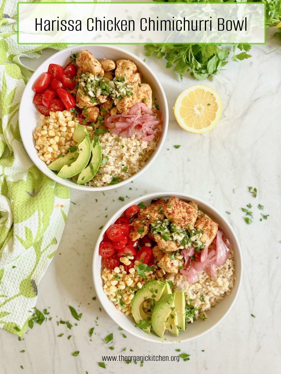 Two Harissa Chicken and Chimichurri Rice Bowls on marble surface surrrounded by herbs, dish towlel and lemon wedge