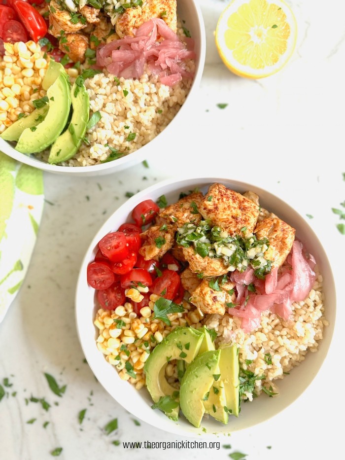 Two Harissa Chicken and Chimichurri Rice Bowls ons white table with a hald lemon