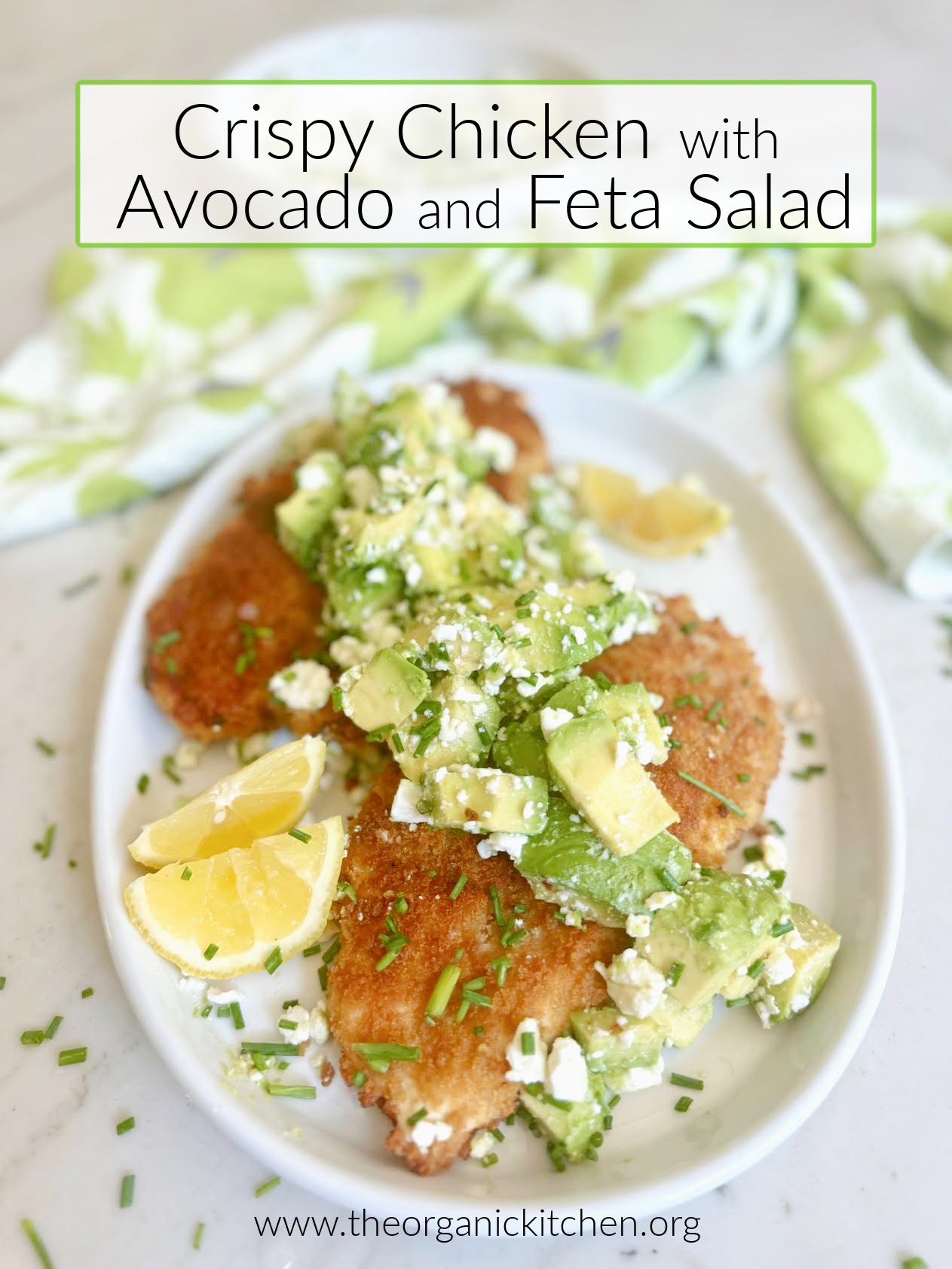 Crispy Chicken with Avocado and Feta Salad on white plate garnished with lemon wedges and chivesa