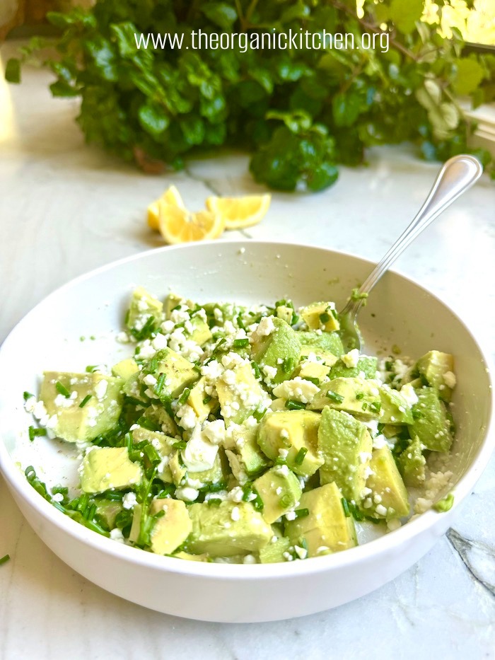 A white bowl filled with avocado and feta salad garnished with chives